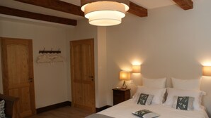 A bedroom with a large bed, wooden doors, and a hanging coat rack. - Les Fréjals (Compeyre)