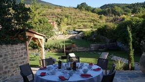 An outdoor dining area with stone walls, a pergola, and a view of a hillside. - Les Fréjals (Compeyre)