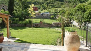 A stone patio with a large vase, a stone wall, and a view of a green lawn and a red building in the distance. - Les Fréjals (Compeyre)
