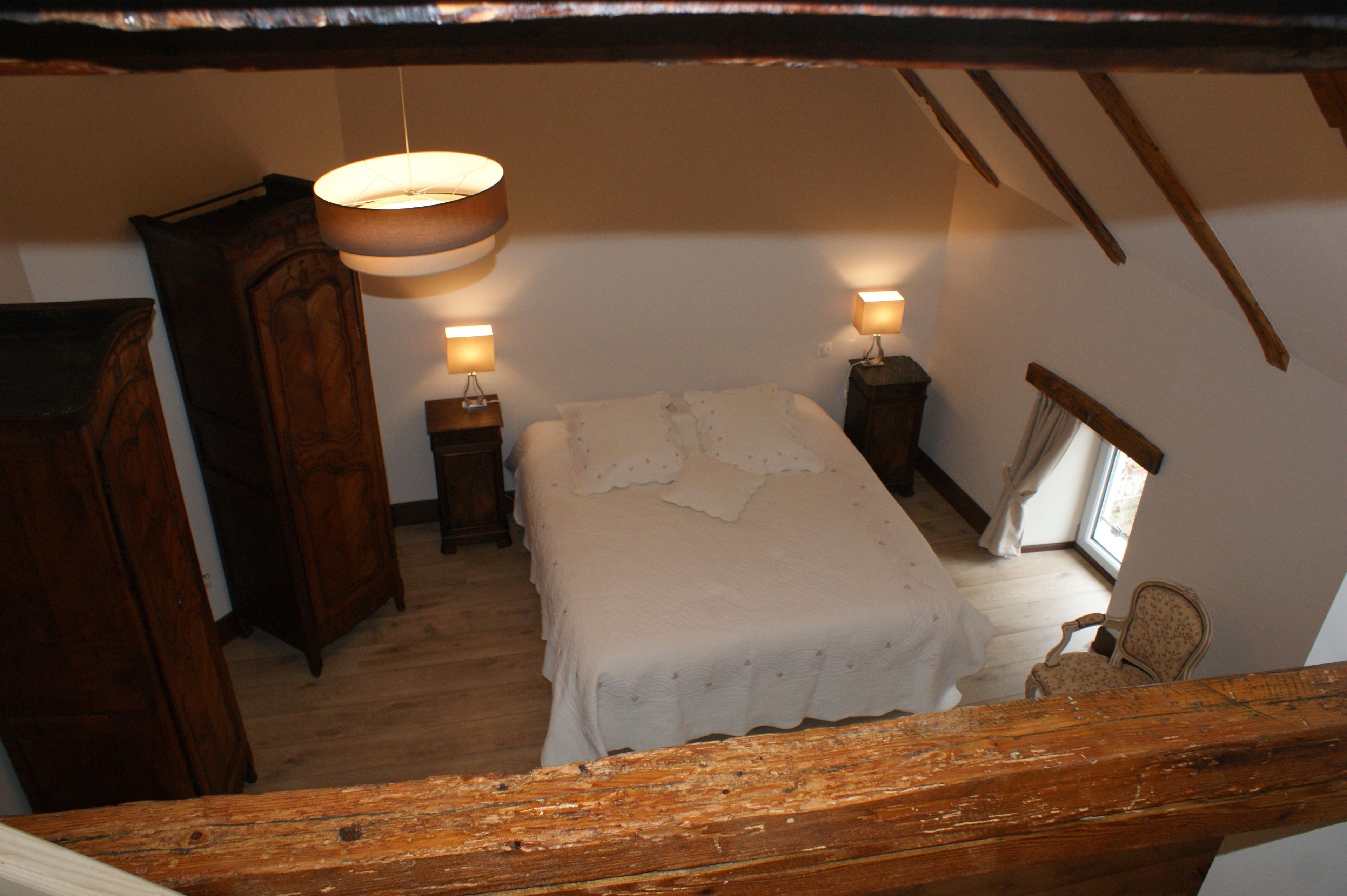 Un dormitorio con una cama, dos mesitas de noche, un armario de madera y una silla.