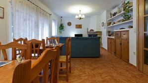 Un coin repas avec des chaises et une table en bois, un canapé bleu et un espace cuisine avec des armoires et des étagères en bois.