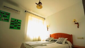 Une chambre à coucher comprenant un lit, une table de chevet, une lampe et un climatiseur fixé au mur.