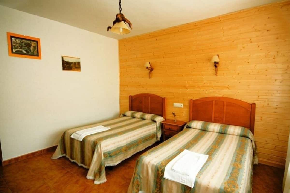 A room with two single beds, wooden walls, and a hanging light fixture.