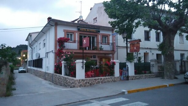 Un bâtiment sur lequel on peut lire l’inscription « Hostal Rio Mundo ». Il possède un balcon orné de fleurs rouges et une base en pierre.