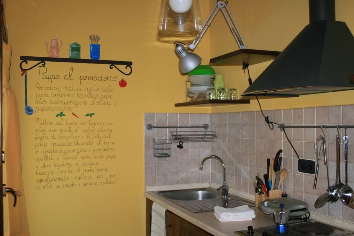 Keittiössä on pesuallas, liesi ja erilaisia keittiövälineitä. Yhdellä seinällä on italialaisella kirjoitettu resepti.