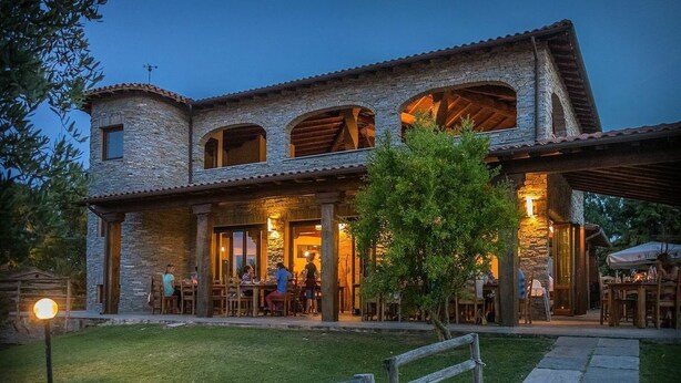 A stone building with a patio area, outdoor seating, and a well-lit entrance. - Vento di Maremma (Grosseto)