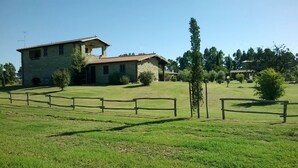 A stone building with a tiled roof, surrounded by a grassy field and a wooden fence. - Vento di Maremma (Grosseto)