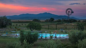 A pool area with a windmill, surrounded by trees and open fields. - Vento di Maremma (Grosseto)