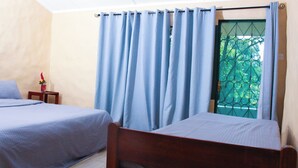 A room with two single beds, a small table with a vase, and a window with blue curtains. - Savage Wilderness - Hostel (Sagana)