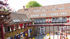 Une cour avec un bâtiment jaune dont la façade est rouge et blanche, un mur de pierre et un portail en métal.