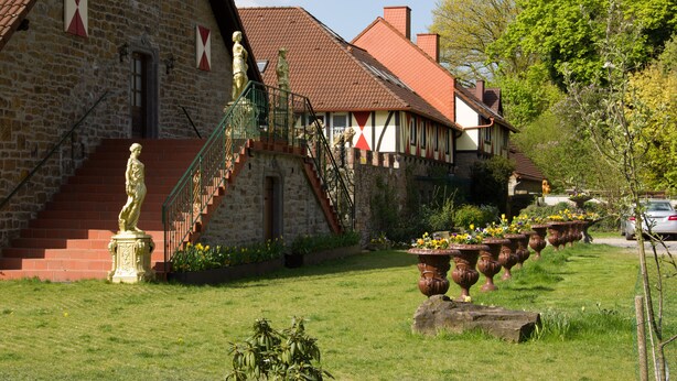 Un bâtiment en pierre avec un toit recouvert de tuiles rouges, un escalier et des statues à l’extérieur.