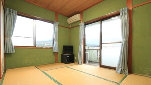 Ein Raum mit Tatami-Matten, einem Fernseher, Schiebetüren und Blick ins Freie.