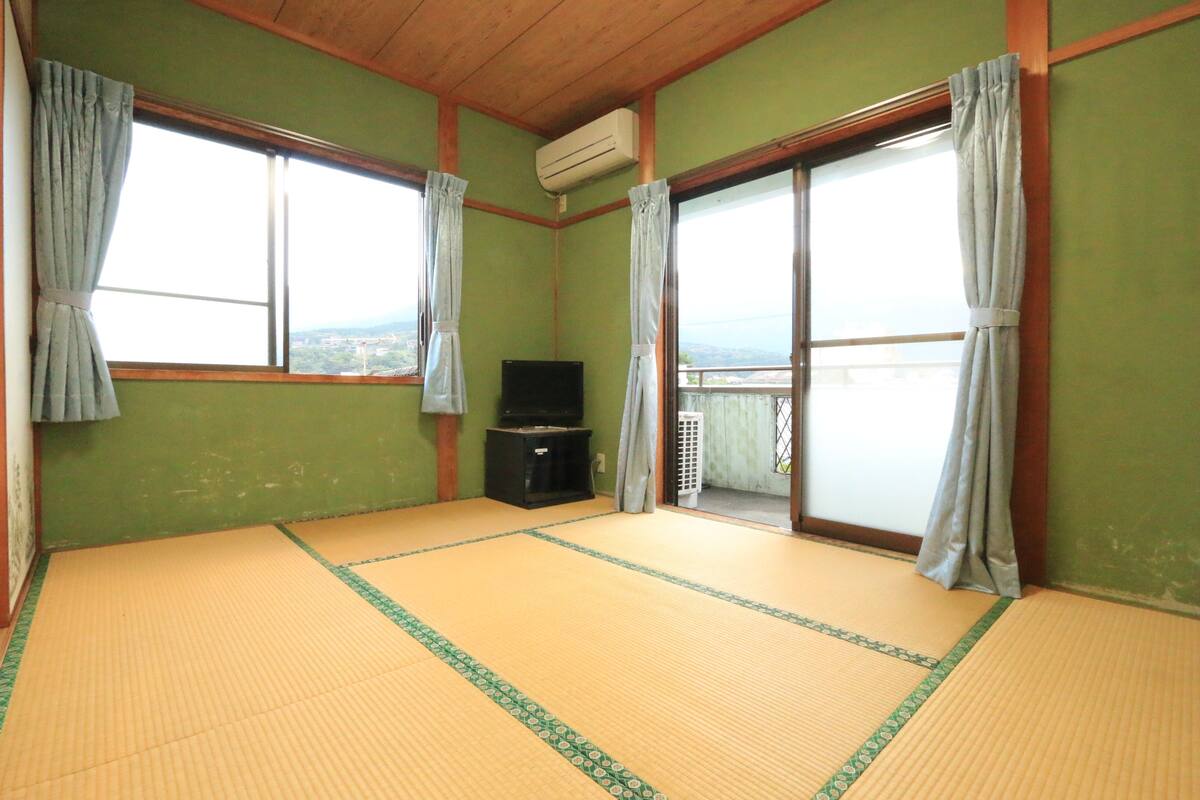 Ein Raum mit Tatami-Matten, einem Fernseher, Schiebetüren und Blick ins Freie.