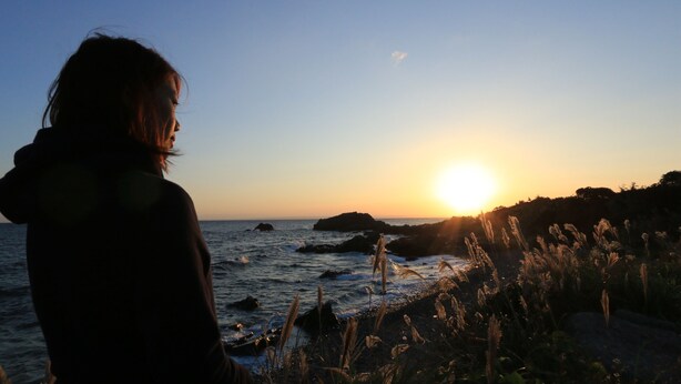 Eine Person steht am Meer bei Sonnenuntergang.