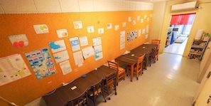 Ein Klassenzimmer mit einer an Lehrmaterialien befestigten Schwarzwertafel, einem langen Holztisch und mehreren Stühlen.