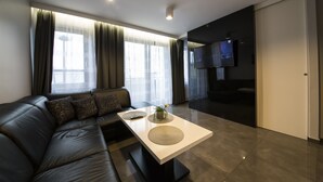 Un salon moderne avec un canapé en cuir noir, une table basse blanche et un téléviseur à écran plat fixé au mur.
