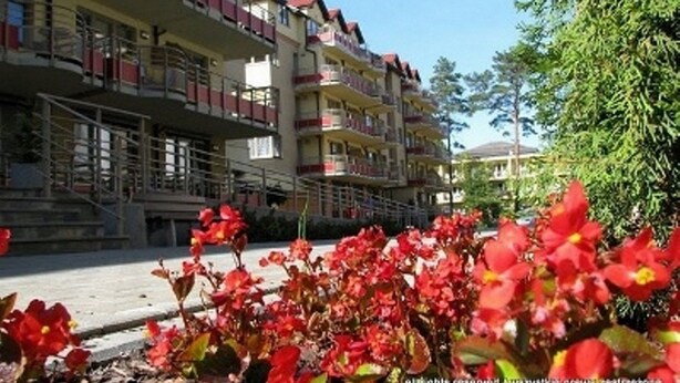 Un hôtel à plusieurs étages, doté de balcons et d’un jardin agrémenté de fleurs rouges.