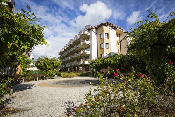 A multi-story residential building with balconies, surrounded by greenery and a paved courtyard.