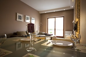 A dining area with a glass table, plates, and wine glasses. There is a sofa and a window in the background.