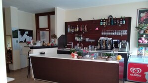 Un espace bar comprenant un comptoir, des étagères remplies de bouteilles et un réfrigérateur.