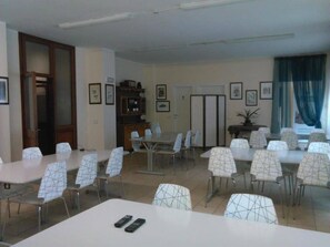 Une salle de conférence équipée de plusieurs tables et chaises, d’un buffet en bois et de tableaux encadrés accrochés aux murs.