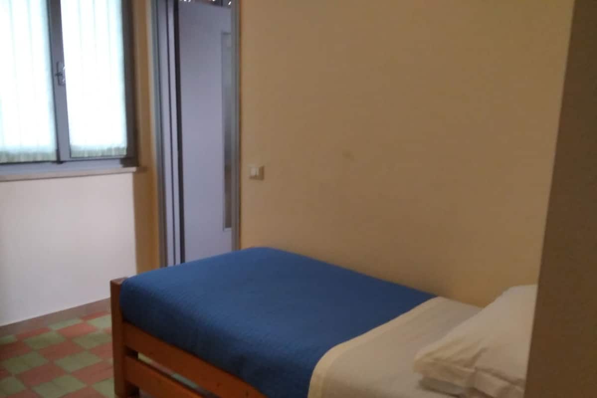 Ein Einzelbett mit blauer Matratze und weißen Kissen in einem Zimmer mit kariertem Fußboden.
