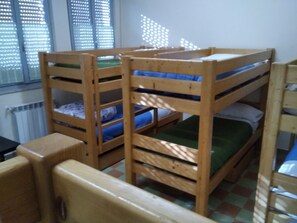 Une chambre avec un lit superposé, un radiateur et une fenêtre équipée de stores.
