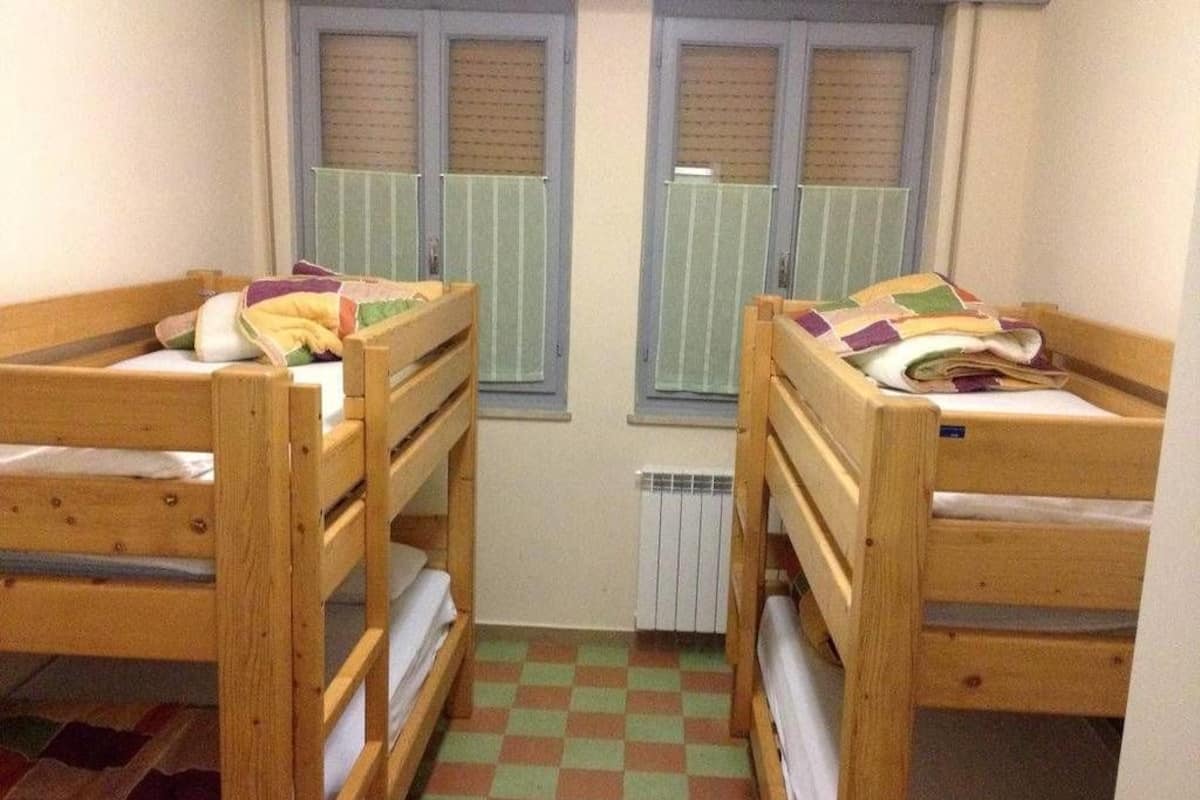 Ein Zimmer mit zwei Holzbettstühlen, einem Heizkörper und einem Fenster mit Jalousien.