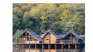 Des cabanes en bois aux toits de chaume, construites sur pilotis au-dessus de l’eau, entourées d’une forêt dense.