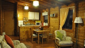L’intérieur d’un chalet accueillant, avec une table à manger en bois, des chaises, un canapé et une fenêtre agrémentée de rideaux.