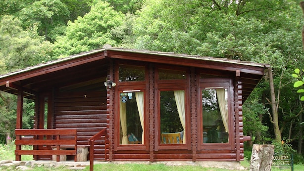 Une cabane en bois dotée d’un porche, d’un banc et d’une pancarte indiquant qu’elle fait partie d’un lieu de villégiature à la campagne.