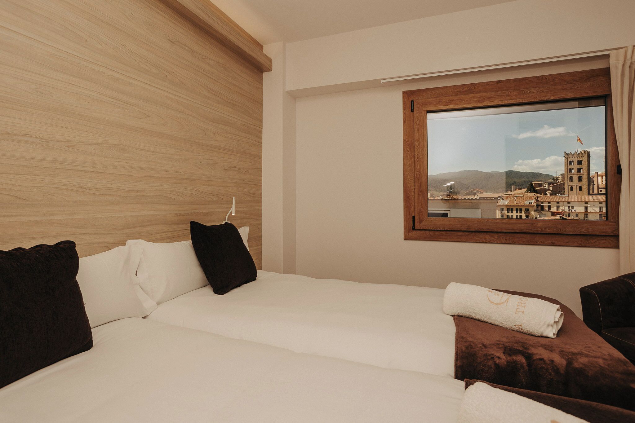 Une chambre d’hôtel avec un lit, des oreillers, une fenêtre donnant sur un immeuble et une tête de lit en bois.