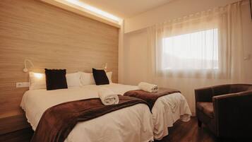 A hotel room with a wooden headboard, two beds with brown bedding, a chair, and a large window with sheer curtains.