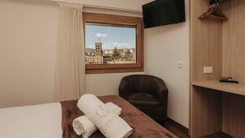 A hotel room with a bed, a chair, a TV, and a window with a view of buildings.