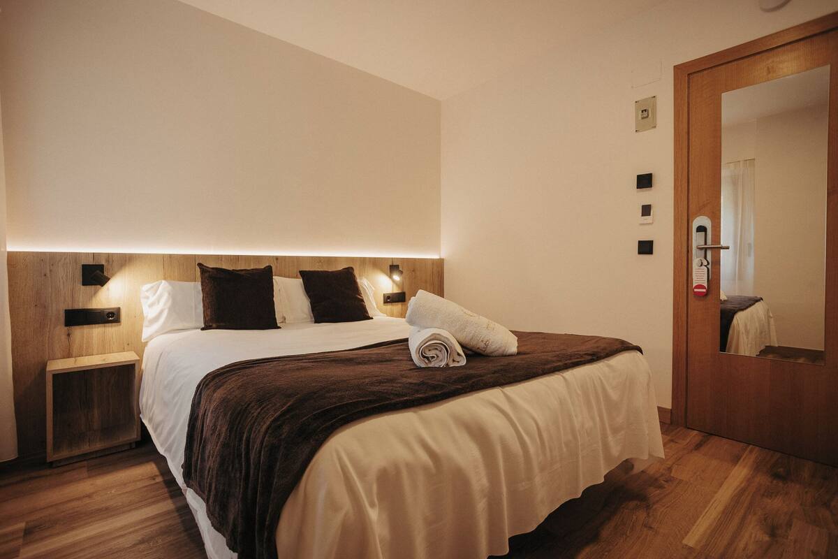 A hotel room with a bed, wooden headboard, bedside tables, a mirror, and a door.