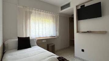 Una habitación de hotel con cama, televisor montado en la pared, ventana con cortinas y una mesita de noche.