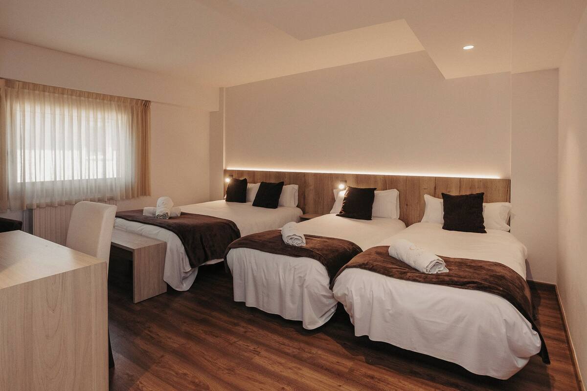 A hotel room with three beds, a desk, and a chair.