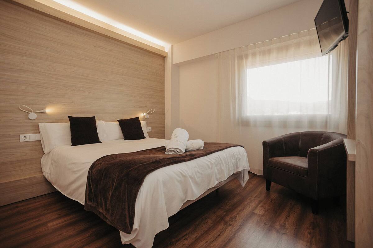 A hotel room with a bed, a chair, a TV, and a window with curtains.
