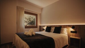 A hotel room with a bed, a window with curtains, a nightstand, and a wall-mounted light fixture. - La Trobada Hotel Sport (Ripoll)