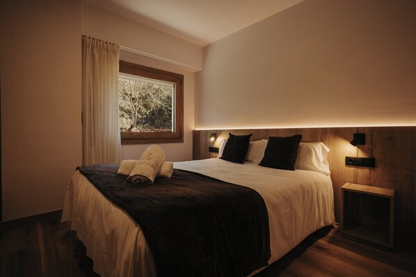 Habitación de hotel con cama, ventana con cortinas, mesita de noche y lámpara de pared.