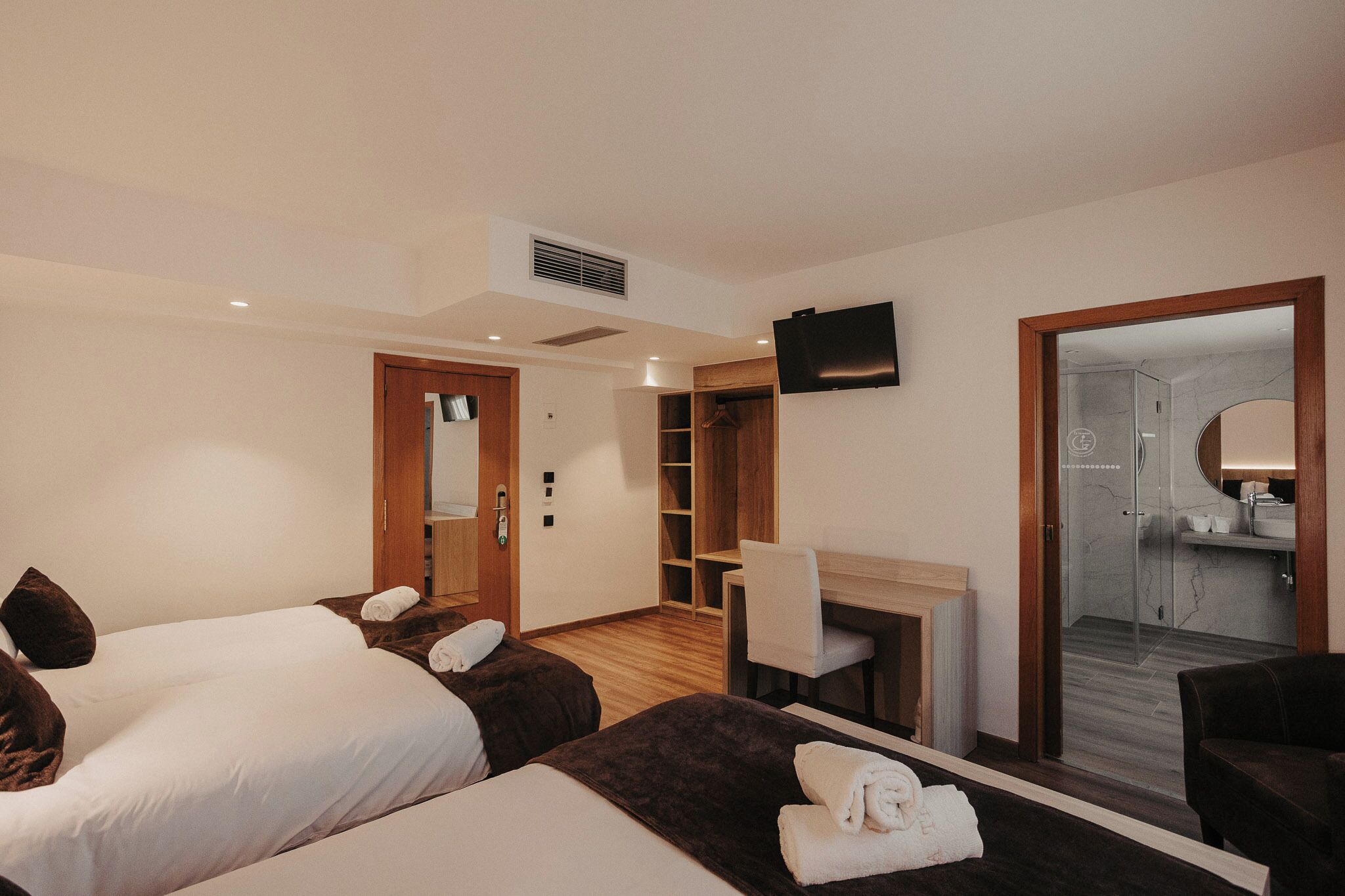 Hotelkamer met twee bedden, een bureau, een stoel, een televisie en een badkamer met douche en wastafel.