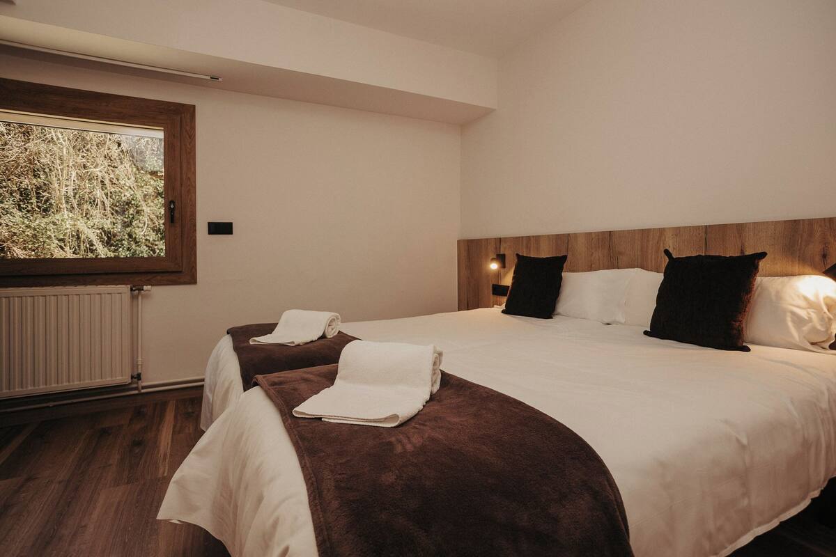 A hotel room with two beds, a large window, a wooden headboard, and a radiator.