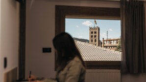 A room with a large window overlooking a building with a tower and a flag. - La Trobada Hotel Sport (Ripoll)