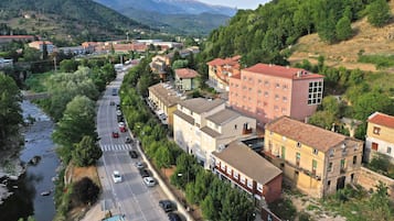 Un pueblo a orillas del río, con edificios a lo largo de la carretera, un puente y montañas al fondo.