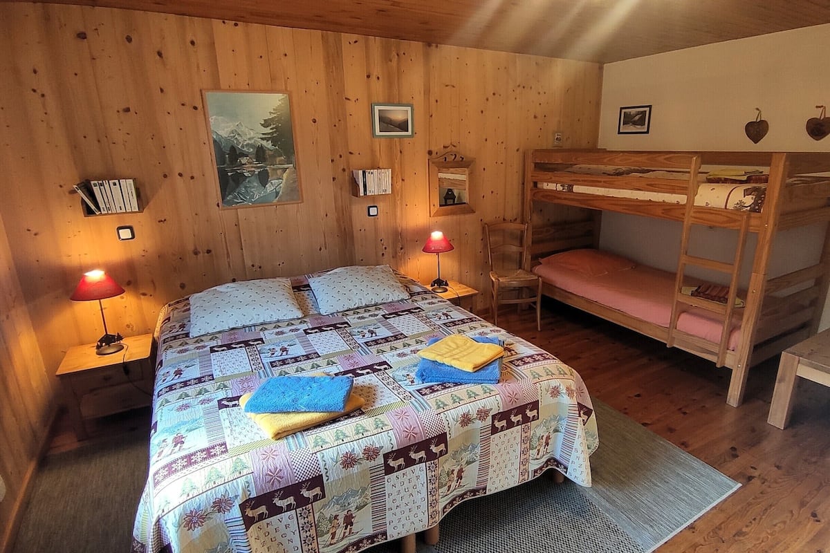 Una habitación de cabaña acogedora con una cama nido de madera, una colcha acolchada, dos lámparas de noche y cuadros en las paredes.