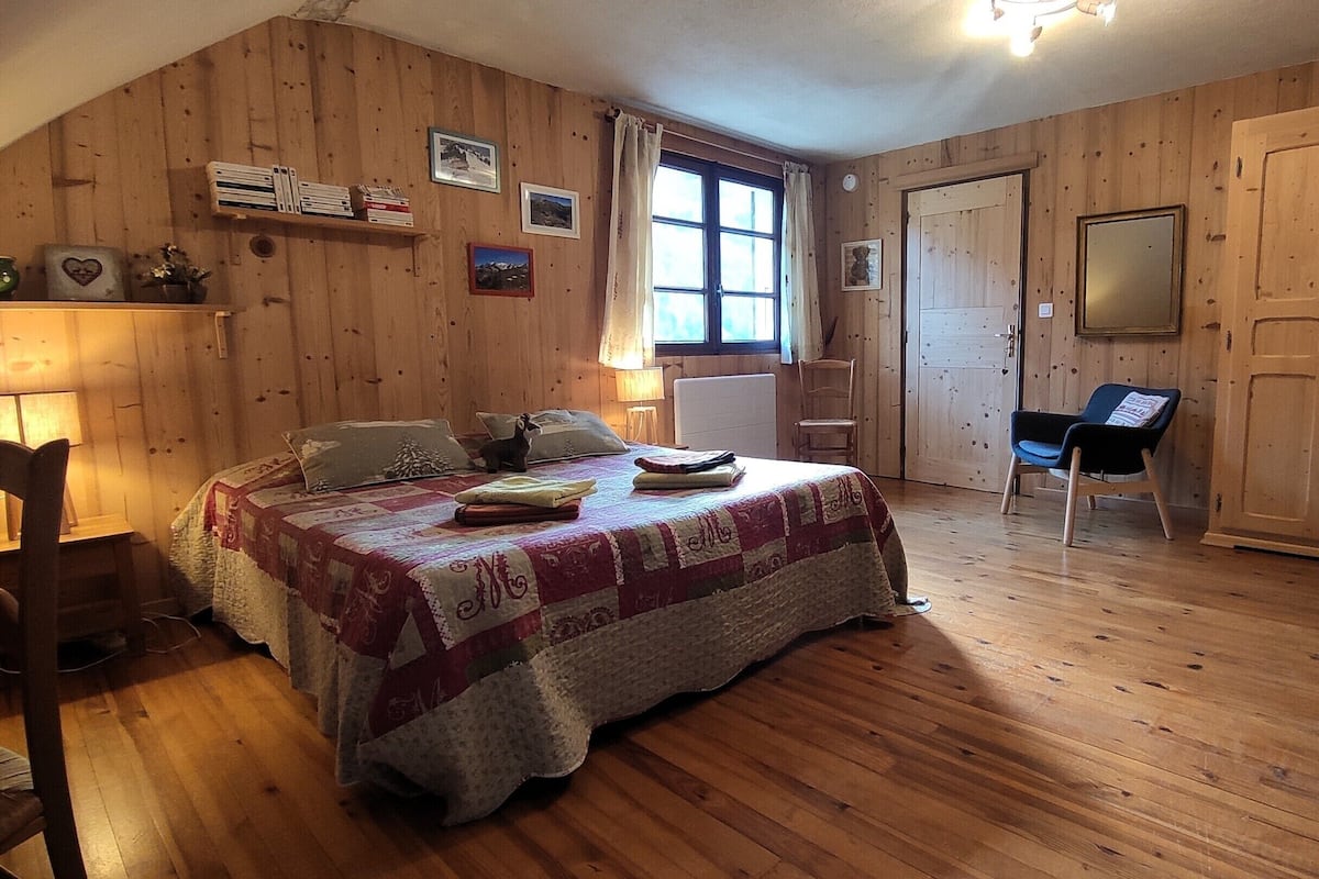 Una habitación acogedora con piso de madera, una cama con colcha, una silla y un escritorio con lámpara.