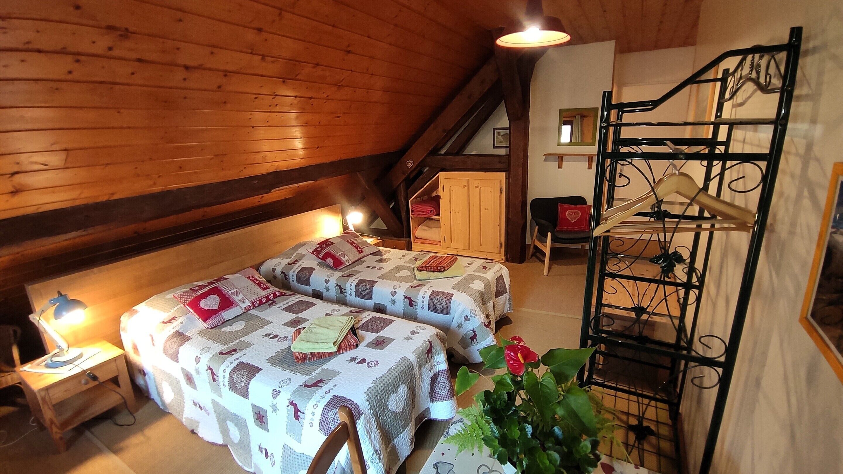 Ein gemütliches Schlafzimmer im Dachgeschoss mit zwei Betten, einer Holzbalkendecke, einem kleinen Schreibtisch und einem Hängesessel.