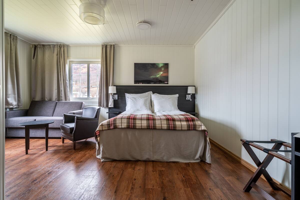 Ein Hotelzimmer mit Bett, einer Couch, einem Sessel, einem kleinen Tisch und einem Fenster mit Vorhängen.