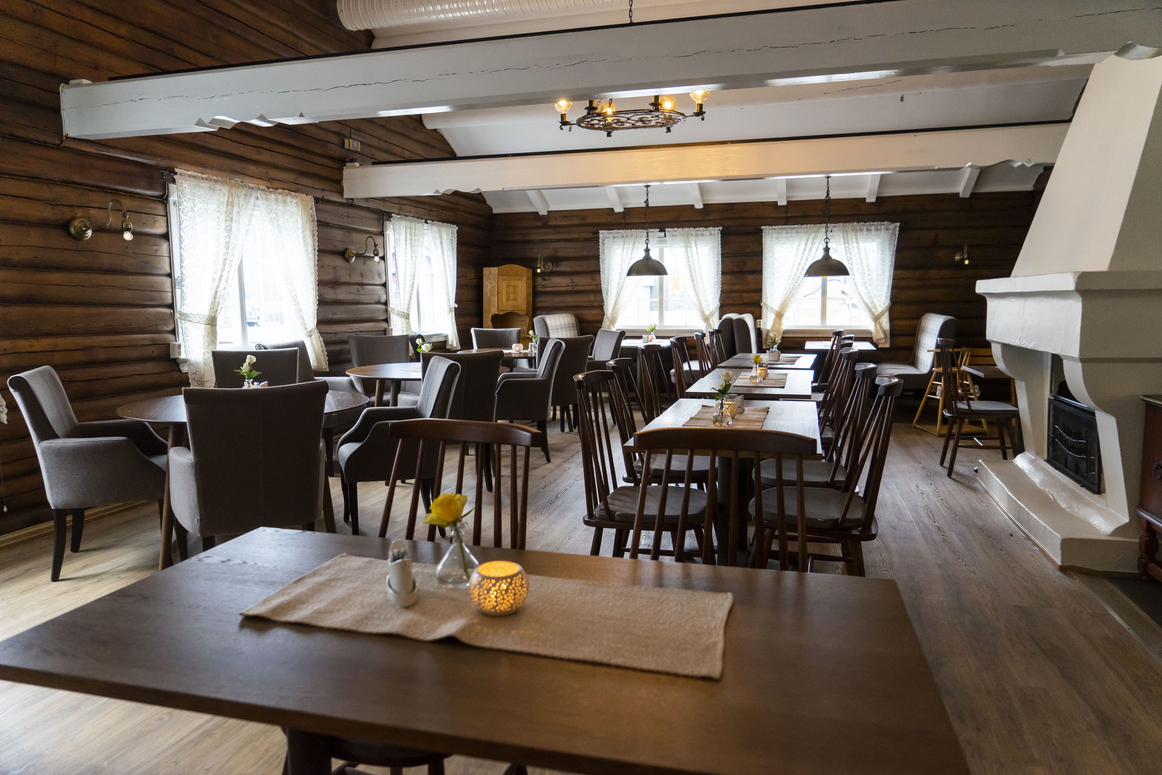A cozy dining area with wooden walls and tables, featuring a fireplace and pendant lights.