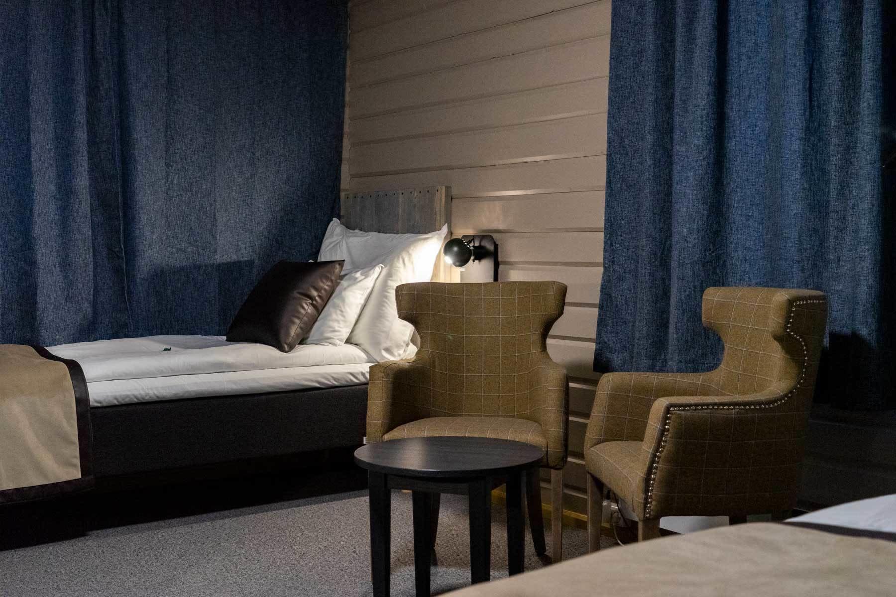 Una habitación con una cama, dos sillones, una mesita y una lámpara.
